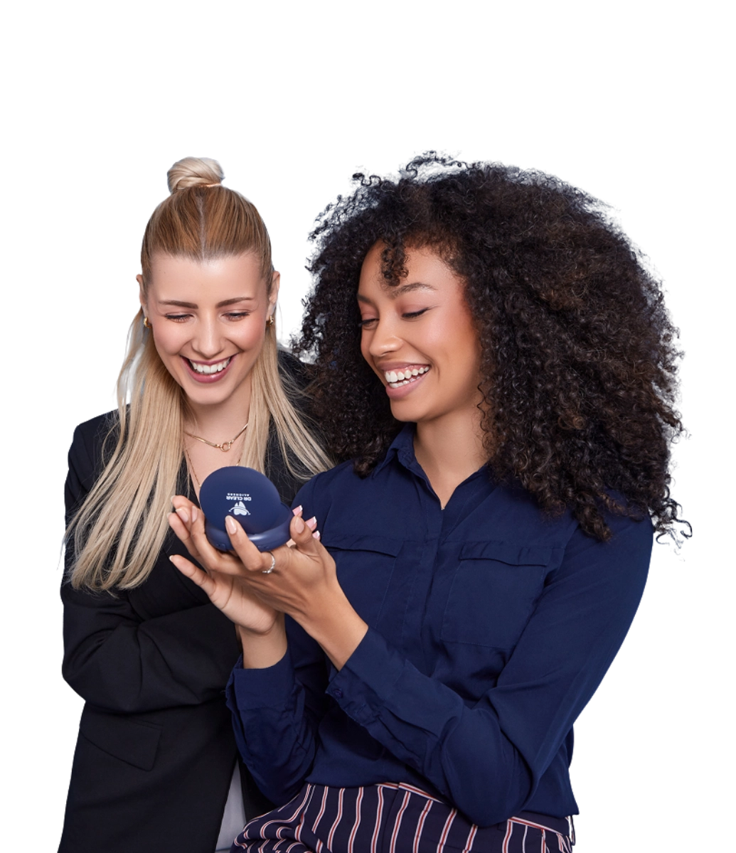 Two women smiling with clear aligners and Dr Clear Aligners case on bed